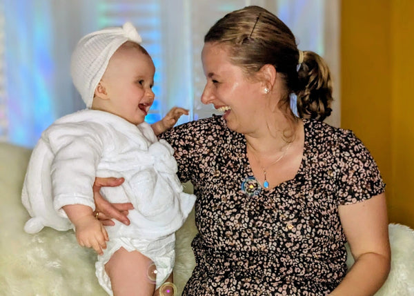 Woman holding a baby wrapped in white cloth, both smiling.